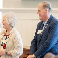 Marcia Haas standing up by podium, addressing crowd with microphone while former President Haas stands next to her smiling